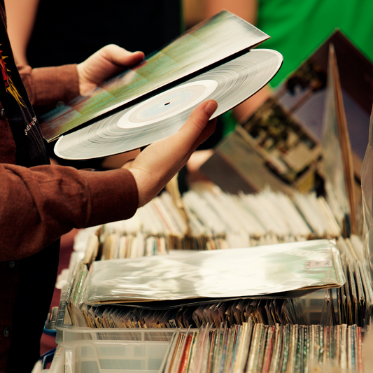 A vinyl record sits on top of some secondhand record cover spines.